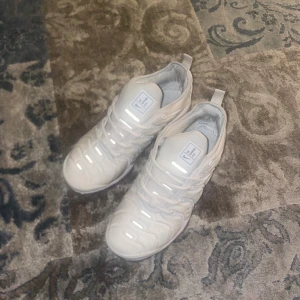 Nike Vapormax vita sneakers - Nike Vapormax sneakers i helvitt med transparent sula och coolt mönstrad ovandel. Skorna har snörning och en modern, sportig look med tydlig Nike-logga på plösen och Vm Air-märke bak. Perfekta för dig som gillar streetstyle och vill sticka ut.