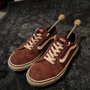Vinröda Vans Old Skool sneakers - Säljer ett par klassiska Vans Old Skool sneakers i vinrött mocka och textil med vita detaljer och snörning. Skorna har den ikoniska vita sidan, vit sula och gummisula med rutmönster undertill. Perfekta för dig som gillar streetwear och skate. Bra skick 