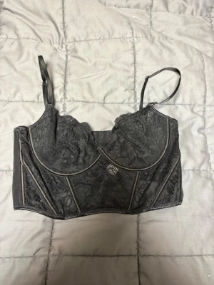 Svart spetstopp från her[body] - Säljer en svart topp från her[body] i storlek M. Toppen har tunna axelband, vackra spetsdetaljer och markerade sömmar framtill. Den stängs med hyskor bak och har en croppad passform 