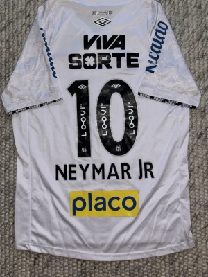 Santos Neymar Jr matchtröja Umbro S - Santos FC matchtröja med Neymar Jr och nummer 10 på ryggen. Tröjan är vit med svarta och gula detaljer, flera sponsorer och klubbmärke på bröstet. Tillverkad i lätt polyester, perfekt för fotboll eller samling. Officiell Umbro-produkt. Bara att fråga om ni vill ha fler bilder eller undrar något 🤝