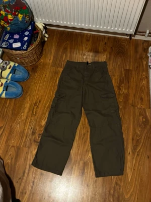 Olivgröna cargobyxor från Divided H&M - Säljer ett par olivgröna cargobyxor från Divided H&M i storlek 38. Byxorna har flera praktiska fickor på sidorna och en loose passform med raka ben. Perfekta för en chill och avslappnad stil. 