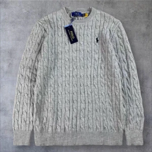 Grå kabelstickad tröja Polo Ralph Lauren - Säljer en klassisk grå kabelstickad tröja från Polo Ralph Lauren. Tröjan har rund halsringning, ribbade muddar och den ikoniska broderade loggan på bröstet. Perfekt till höst och vinter för en stilren look.