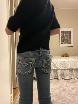Blå bootcut jeans med detaljerade fickor - Säljer ett par blå bootcut jeans med låg midja och snygga, broderade bakfickor med knappar. Jeansen är i bra skick och kommer från Gina tricot