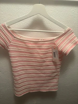 Rosa och vit randig topp från Nelly - Söt stickad topp från Nelly i rosa och vitt med horisontella ränder. Modellen är offshoulder med korta ärmar och har en croppad passform. Perfekt för sommarens alla tillfällen och ger en fräsch och ungdomlig vibe.