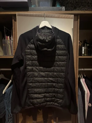 Svart hybrid Cardigan från Peak Performance - Säljer en svart hybrid cardigan från Peak Performance med quiltad front och rygg, samt mjuka ärmar och sidor. Har haft den i min ägo i 1 år och har funkat för både höst/vår. Sitter slimfit. Säljer den då jag vuxit ur den och har skaffat annan cardigan. 