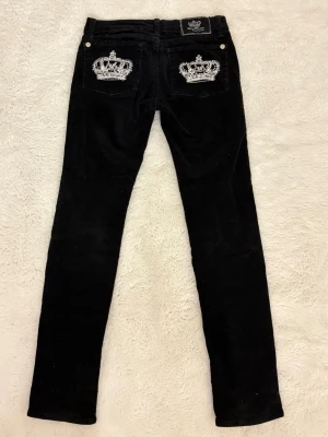 Svarta Victoria Beckham jeans lågmidjade - Svarta manchesterjeans från Victoria Beckham slim passform och supercoola diamant kronor på bakfickorna. ❗️🌸byxorna är köpta second hand men har ej kommit till användning och säljs därför. Storlek är w27 men dom är stretchiga så jag skulle säga att de passar mellan XS/S