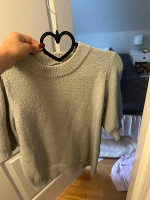 Ljusgrön stickad tröja med kort ärm - Mysig ljusgrön stickad tröja med korta ärmar och ribbad rund hals. Perfekt till lager på lager och enkel att styla med olika outfits. Tröjan har en mjuk struktur och avslappnad passform.