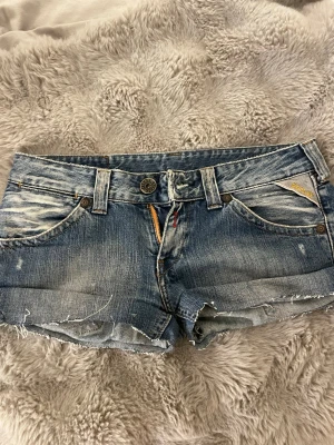 Blå jeansshorts från Replay - Säljer ett par riktigt snygga låg midjade blå jeansshorts från Replay med slitna detaljer och råa kanter. Perfekta för sommaren och passar till allt! De är ungefär i storlek S men passar en liten M skulle jag säga!💕säljer pga att de inte passar. De är även uppsydda och sedan uppvikta men inget syns!! 