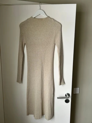 Beige ribbad långklänning NA-KD - Säljer en beige ribbad långklänning från NA-KD i storlek M. Klänningen har lång ärm, rund halsringning och är stickad i ett mjukt material som ger en snygg och bekväm passform. Perfekt för dig som gillar stilrena och enkla plagg.
