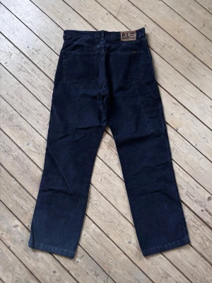 Vintage Ralph Lauren loosefit manchesterbyxor marinblå, strl 32/32 - Säljer ett par mörkblå manchesterbyxor från Polo Jeans Co. Ralph Lauren. Byxorna har raka ben, klassiska snedställda fickor fram och bakfickor samt en extra sidficka. Tydlig RL-läderpatch bak i midjan och snygg vintagekänsla.