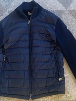 Mörkblå dunväst från Moncler - Snygg mörkblå caridgan från Moncler med quiltad framsida och två dragkedjefickor. Jackan har en hög krage och Moncler-logga på axeln. Materialmix med polyester och stickade detaljer ger en exklusiv känsla. Perfekt för lager-på-lager och streetstyle. pris kan ej diskuteras, äkta jacka  kvitto finns, fråga frågor vid intresse skick 8/10