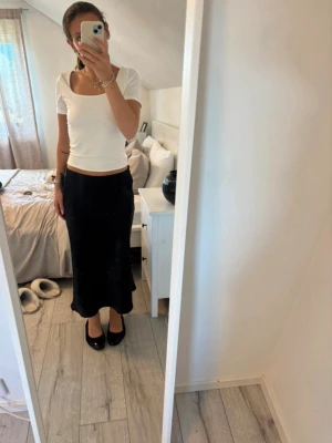 Svart långkjol i satin - Säljer en svart långkjol i glansigt satinmaterial. Kjolen har en rak och enkel passform som faller snyggt längs benen. Perfekt att styla med både sneakers och klackar. Superenkel att matcha med olika toppar!