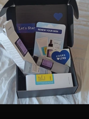 COSRX ansiktskit med toner och rengöring - Kit från COSRX med Low pH Good Morning Gel Cleanser i vit tub med blå och gul etikett samt ansiktstoner i genomskinlig flaska med lila etikett. Perfekt för dig som vill ha en enkel hudvårdsrutin. Produkterna är i smidiga plastförpackningar.