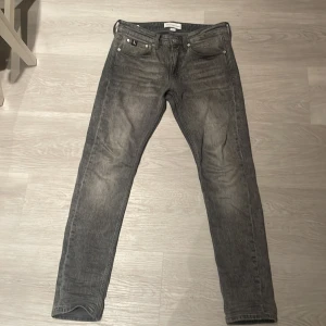 Grå jeans från Calvin Klein - Snygga grå jeans från Calvin Klein Jeans med klassisk CK-logga på bakfickan och metallknapp med CK-detalj fram. Jeansen har fem fickor, raka ben och en tvättad finish som ger en cool, lite sliten look. Perfekt för dig som gillar stilrena och tidlösa jeans.😇storleken: w28 Xl32