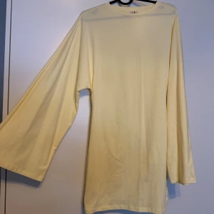 Ljusgul långärmad klänning från Nelly - Ljusgul långärmad klänning från Nelly med riktigt breda ärmar och enkel, rak passform. Mjuk och tunn i bomullsmaterial. Lite lätt genomskinlig. Aldrig använd. 