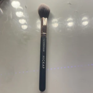 Hickap 114 Tapered Blush borste - Snygg sminkborste från Hickap, modell 114 Tapered Blush. Borsten har ett svart handtag med vit logga och ett elegant roséguldfärgat fäste. Mjuka syntetiska borststrån, perfekt för applicering av rouge eller bronzer. Helt oanvänd 