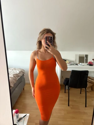 Orange tight klänning med smala axelband - Säljer en snygg orange klänning med smala axelband och figurnära passform. Klänningen är ärmlös och har en enkel, stilren design som sitter riktigt bra på kroppen. Perfekt för dig som gillar färgstarka plagg och vill sticka ut lite extra.