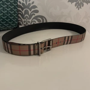 Rutig skinnbälte från Burberry - Säljer ett snyggt bälte från Burberry i klassiskt rutigt mönster med beige, bruna, svarta och röda toner.