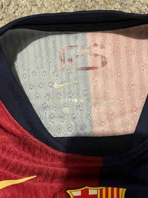 FC Barcelona Lamine Yamal tröja , Travis scott - Säljer en officiell FC Barcelona matchtröja från Nike med Lamine Yamal och nummer 19 på ryggen. Tröjan har klassisk halva röd och halva marinblå design, korta ärmar, gul text och detaljer, samt klubbmärke på bröstet. Materialet är lätt och andas, perfekt för fotboll.