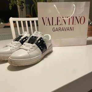 Valentino Garavani Rockstud sneakers - Snygga vita sneakers från Valentino Garavani med svarta detaljer och ikoniska Rockstud-nitar. Skorna har rund tå, snörning och platt sula. Tillverkade i skinn med cool kontrast mellan vitt och svart. Perfekta för dig som gillar lyxiga street vibes och edgy detaljer.
