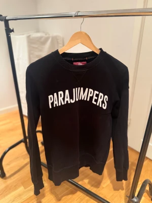 Svart fleece-tröja Parajumpers S - Svart fleece-tröja från Parajumpers i storlek S med vit logotyp på bröstet och snyggt broderat märke på ärmen. Tröjan har även orangea sömmar. Perfekt för dig som gillar streetwear och vill ha något bekvämt. Har använts sparsamt med inga defekter.