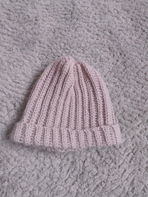 Ljusbeige virkad mössa - Säljer en ljusbeige virkad mössa med uppvikt kant som jag gjort själv. Mössan är handgjord i mjukt garn och har en klassisk, rundad form som sitter skönt på huvudet. Perfekt för kalla dagar och enkel att matcha med din vinterstil.