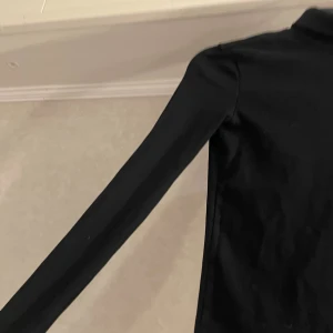 Svart polotröja från Zara - Svart polotröja från Zara i storlek S. Tröjan har lång ärm och en klassisk hög krage som sitter snyggt runt halsen. Materialet är mjukt och stretchigt, perfekt för lager-på-lager. Enkel och stilren design utan mönster eller detaljer.