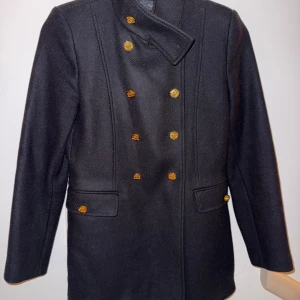 Svart skepparkavaj med guldknappar från Zara - Stilren svart skepparkavaj med dubbelknäppning och snygga guldknappar framtill. Jackan har hög krage och raka fickor med lock. Perfekt för dig som vill ha en klassisk och tidlös look.