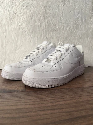 Nike Air Force 1 vita sneakers - Fräscha Nike Air Force 1 sneakers i helvitt skinn med klassisk rund tå och platt sula. Snygga detaljer som perforeringar på tån och metallbricka med 'AF1' på snörningen. Perfekt för dig som gillar cleana och tidlösa sneakers med streetkänsla.
