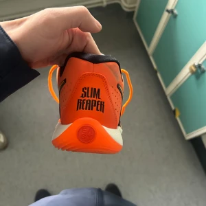 Nike KD Slim Reaper orange sneakers - Säljer ett par Nike KD Slim Reaper sneakers i en riktigt fet orange färg med svarta och gula detaljer. Skorna har snörning, låg profil och en platt sula med coolt mönster undertill. Materialet är syntet och mesh för grym komfort och ventilation. Perfekt för dig som vill sticka ut.