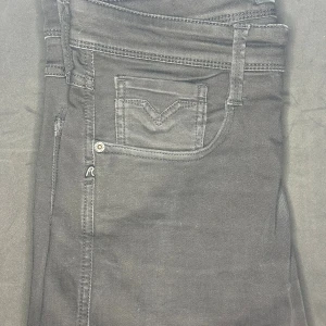 Replay anbass jeans - Svarta jeansbyxor från Replay med klassisk femficksdesign och diskret Replay-logga på myntfickan. Byxorna har raka ben och tydliga sömmar, tillverkade i ett mjukt bomullsmaterial med lite stretch för extra komfort. Perfekta för en stilren och avslappnad look. Storlek 31/32