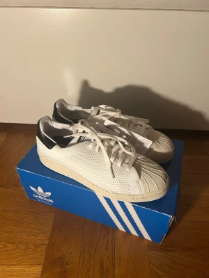 Adidas Superstar 80s PK vita sneakers - Adidas Superstar 80s PK sneakers i vitt med svart häl. Klassisk rund tå och snörning, stickad ovandel i syntetmaterial och ikonisk gummitå. Snygg retrostil med Originals-logga på plösen. Perfekt för dig som gillar tidlös streetwear. (Ordniare pris 1500kr)