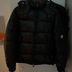  Moncler Maya  - Säljer en snygg svart dunjacka från Moncler. Den är i mycket bra skick och perfekt för vintern.  Den håller värmen bra och ser stilren ut.                                                          Det är ett litet hål inuti jackan som inte syns och går lätt att sy igen. Därför säljer jag den billigare. Som sagt är de lilla hålet inuti jackan.                                                       Jag kan tänka mig att diskutera priset.