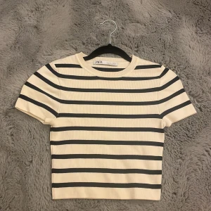 Randig croppad topp från Zara - Säljer en croppad topp från Zara i storlek S. Toppen är vit med svarta ränder, har rund hals och korta ärmar. Materialet är ribbad bomull.