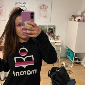 Svart långärmad tröja Isabel Marant - Svart långärmad tröja från Isabel Marant Étoile med ikoniskt tryck i vitt, rosa och lila på bröstet. Tröjan har rund halsringning och är i mjukt, tunt material. Perfekt för dig som gillar stilrena logoplagg med en färgklick.