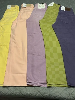 Färgglada raka jeans i olika färger - Fem par raka jeans i trendiga färger: gul, persika, lila, grön med rutmönster och mörklila. Perfekta för dig som vill sticka ut med färg. Jeans i bomullsmix med klassisk femficksdesign och hög midja. Märkena varierar, bland annat Karve.