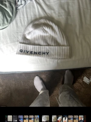 Beige ribbstickad mössa Givenchy - Snygg beige ribbstickad mössa från Givenchy med svart broderad logga framtill och Givenchy-symbol på sidan. Klassisk modell med uppvikt kant, perfekt för att lyfta din streetwear-look.
