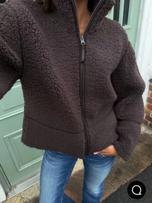 Mörkbrun teddyjacka med dragkedja - Mysig mörkbrun teddyjacka med hög krage och hel dragkedja framtill. Perfekt för kyliga vårdagar och enkel att styla till jeans eller andra byxor.