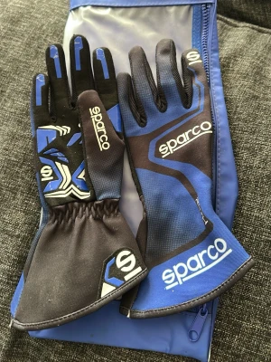 Blå racinghandskar från Sparco - Säljer ett par blå och svarta racinghandskar från Sparco med vita logotyper och detaljer. Handskarna har lång mudd och är designade för motorsport, med greppvänligt material i handflatan och sportig look. Storlek 7 aldrig använda 