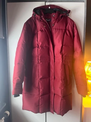 Vinröd lång dunjacka med huva - Snygg vinröd/roströd (superhärlig färg!)  dunjacka från TAKE OFF med lång passform och vadderad design. Jackan har en stor huva, dragkedja och tryckknappar framtill samt två sidofickor. Perfekt för kalla vinterdagar och ger en riktigt skön och varm känsla. Aldrig använd! Storlek L