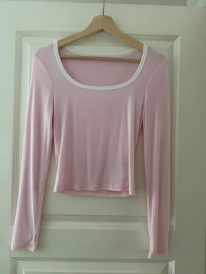 Ljusrosa croppad långärmad topp - Söt ljusrosa croppad topp med långa ärmar och vit kant runt den breda, rundade halsringningen. Mjuk och stretchig känsla. Knappt använd