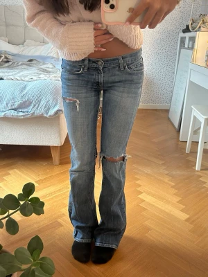 Blå bootcut jeans med slitningar - Snygga blå bootcut jeans med slitningar på låret och knät. Jeansen har låg midja och coola broderade detaljer på bakfickorna. Perfekta för en avslappnad och trendig look. ÄLSKAR men kommer tyvärr inte till användning längre 💕