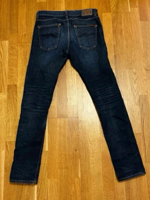 Mörkblåa Nudie Jeans - Snygga mörkblå slim fit-jeans “Lean Dean” – en populär modell från Nudie Jeans. Jeansen har en något tvättad look och är tillverkade i bomull med skön stretch. Ursprunglig storlek är 30x34, men midjan har blivit utvidgad i efterhand (manuellt) till ca 41 cm mätt platt, vilket motsvarar ungefär 32x34.