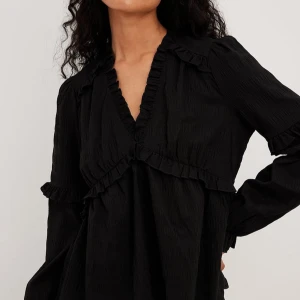 NAKD svart blus med volang - Snygg svart blus med v-ringning och volangdetaljer. Blusen har långa ärmar och en fin passform, perfekt för en stilren look. Tillverkad i ett lätt och bekvämt material. Från Nakd, storlek 34. Nypris 400kr❤️