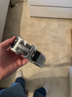 Svart her.mes bälte  - Helt nytt Stilrent svart bälte med ett stort H-format spänne i silverfärg. Bältet har en klassisk design och passar perfekt till jeans eller kostymbyxor. Materialet ser ut att vara skinn och spännet ger en exklusiv känsla. 125cm 