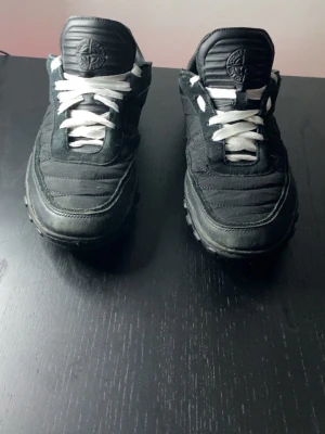 Svarta Stone Island sneakers - Säljer ett par svarta sneakers från Stone Island med vit sula och vita skosnören. Skorna har en låg profil och är tillverkade i en mix av mocka och textil. Klassisk Stone Island-logga på plösen och diskret branding på sidan. Perfekta för en clean streetwear-look. Ny pris runt 2500. Kommer tyvär ej i orginalbox. Pris är diskuterbart