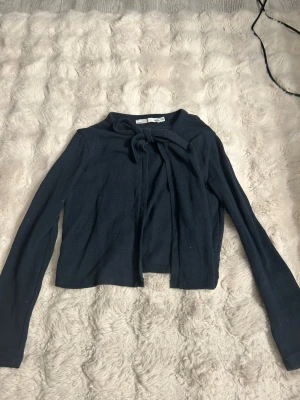 Mörkblå knytkofta från 157 - Mörkblå kofta från 157 med långa ärmar och snygg knytning vid halsen. Kortare modell som passar perfekt till high waist jeans eller kjol. Mjuk och tunn stickning som känns skön mot huden.