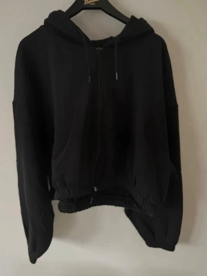 Svart croppad oversized kofta med dragkedja - Svart croppad + oversized kofta med dragkedja. Snörning i midjan på insidan och i huvan. Fint skick. Storlek M!