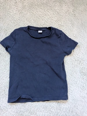 Mörkblå ribbad t-shirt från Lindex  - En enkel och stilren mörkblå t-shirt med ribbad struktur och rund hals. T-shirten har korta ärmar och en klassisk passform som funkar till det mesta. Perfekt basplagg för garderoben.