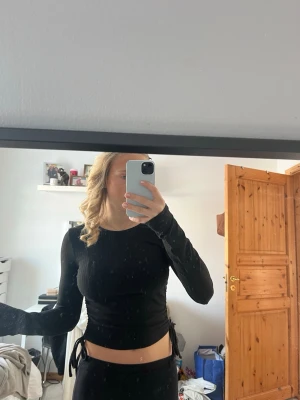 Svart ribbad croppad långärmad topp - Säljer en svart ribbad croppad topp med långa ärmar och knyt-detaljer i sidorna. Mjuk och stretchigt material och sitter tight. Från bubbelroom i storlek S